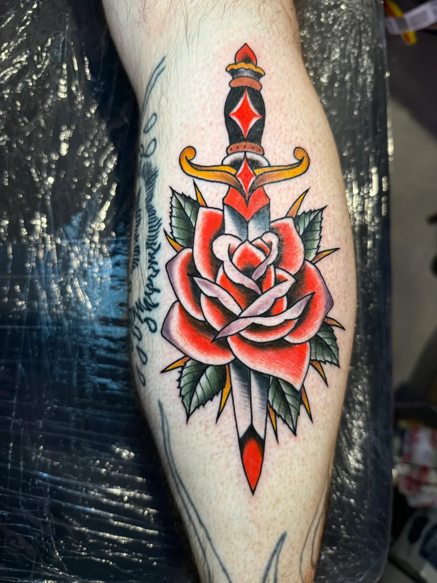 Un pugnale che attraversa una rosa rossa, tatuato sul polpaccio.