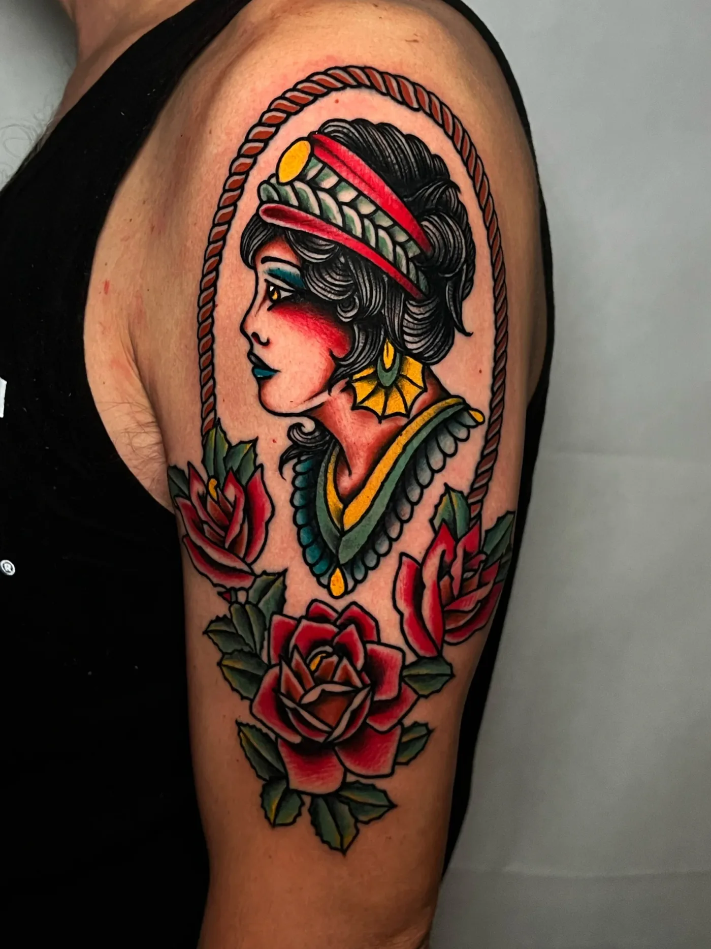 Un volto di donna dentro una cornice di corda, con due rose rosse, sul braccio.
