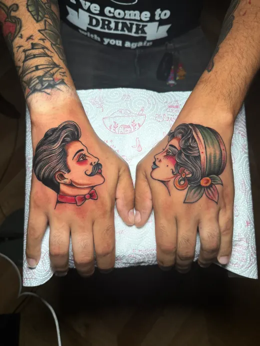Two hands side by side: on the back of each, a portrait — a moustached man and a woman in a headscarf.