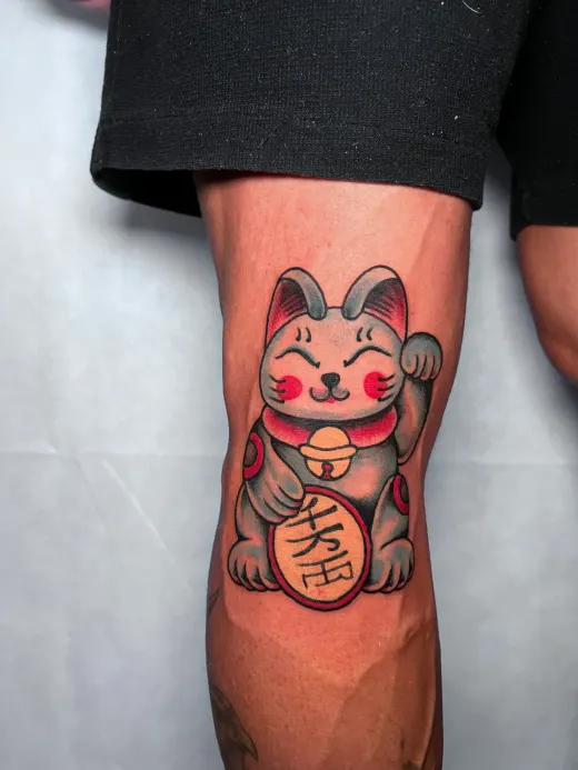 A Japanese lucky cat with a raised paw, on the knee.