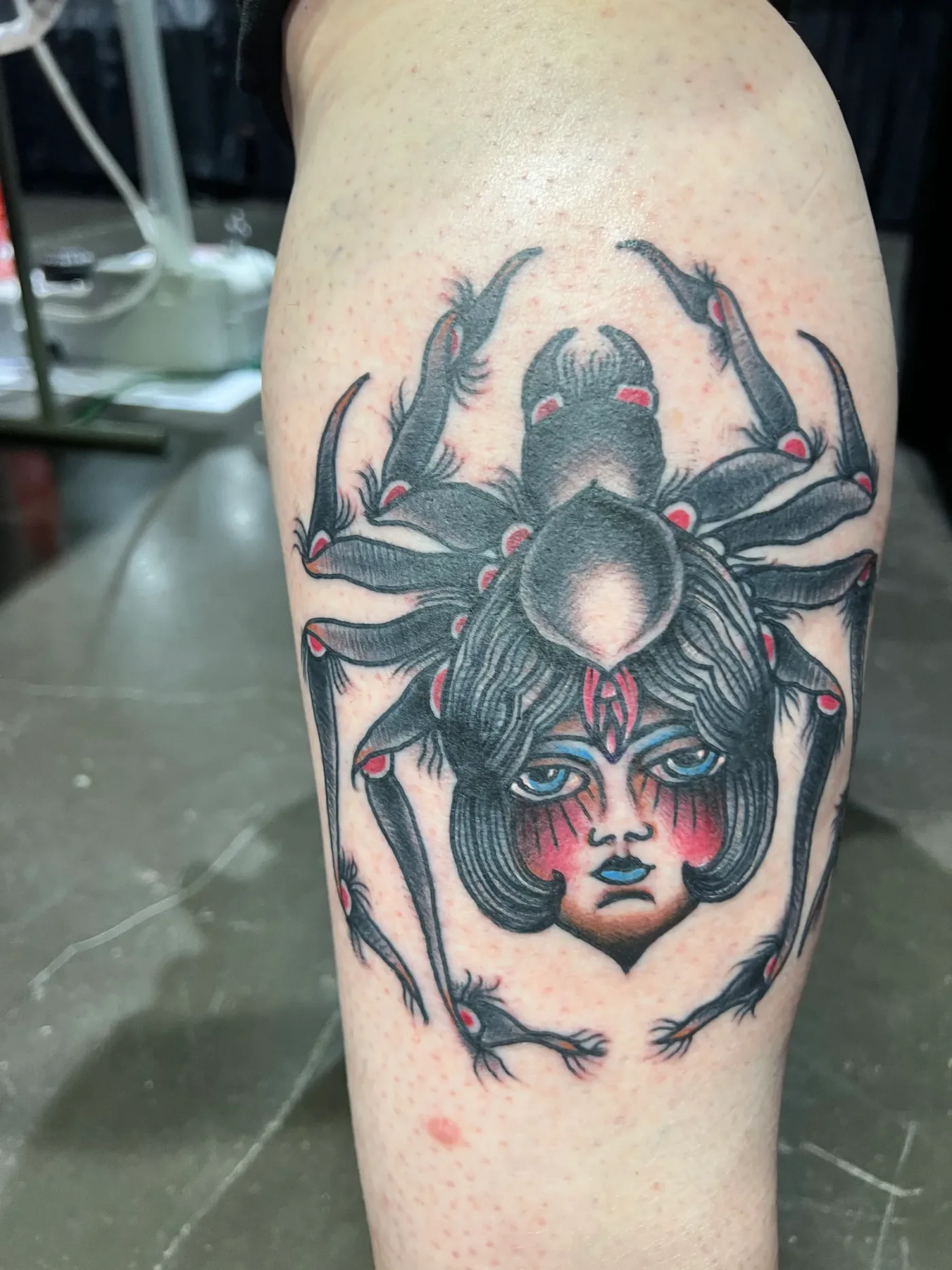 Un ragno con al centro il volto di una donna, in nero e grigio, sulla gamba.